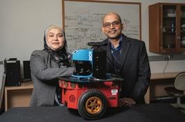 Two researchers stand in front of a red robot